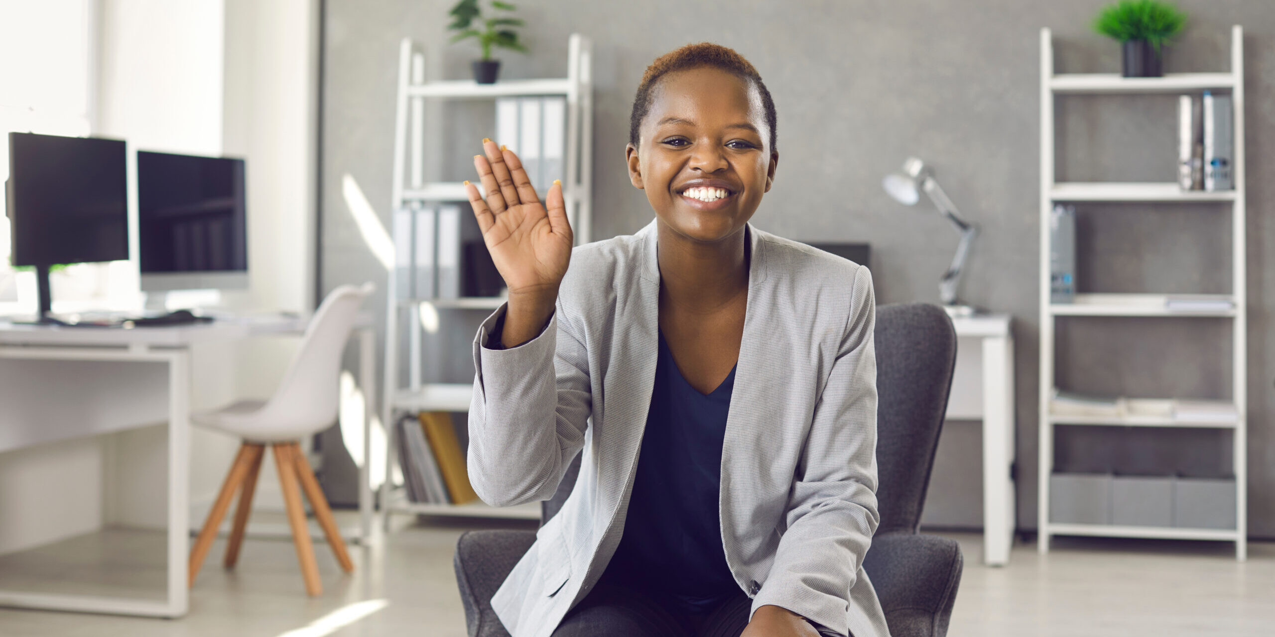 Black,Woman,Sitting,In,Office,,Waving,Hand,,Smiling,And,Saying