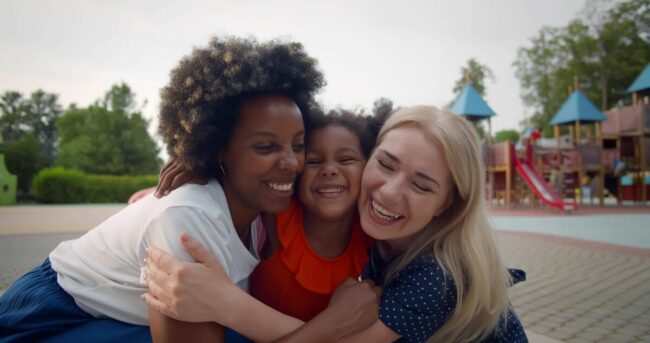 multiethnic-lesbian-couple-adopted-little-daughter-hugging-playground_867394-933