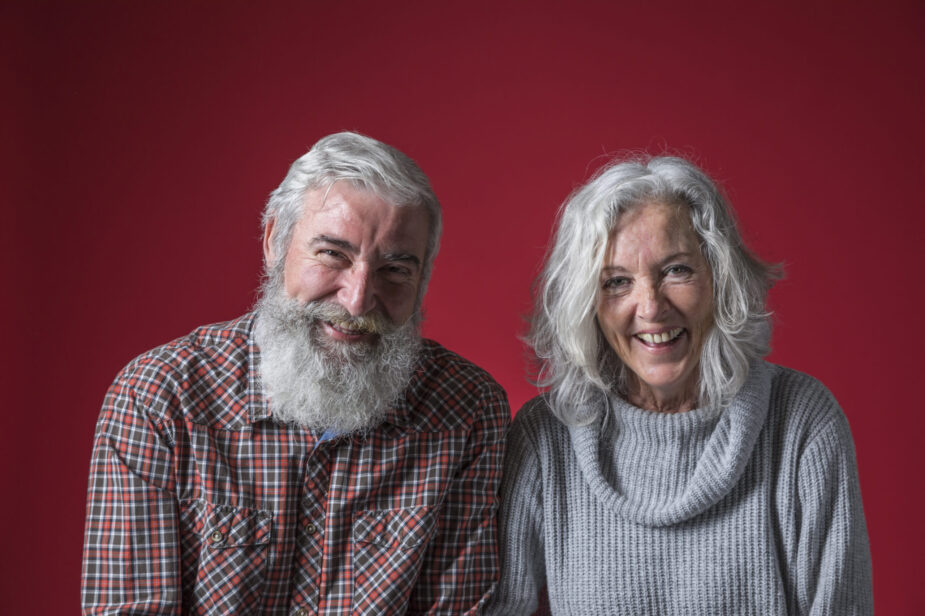 portrait-smiling-senior-couple-with-grey-hair-against-red-background